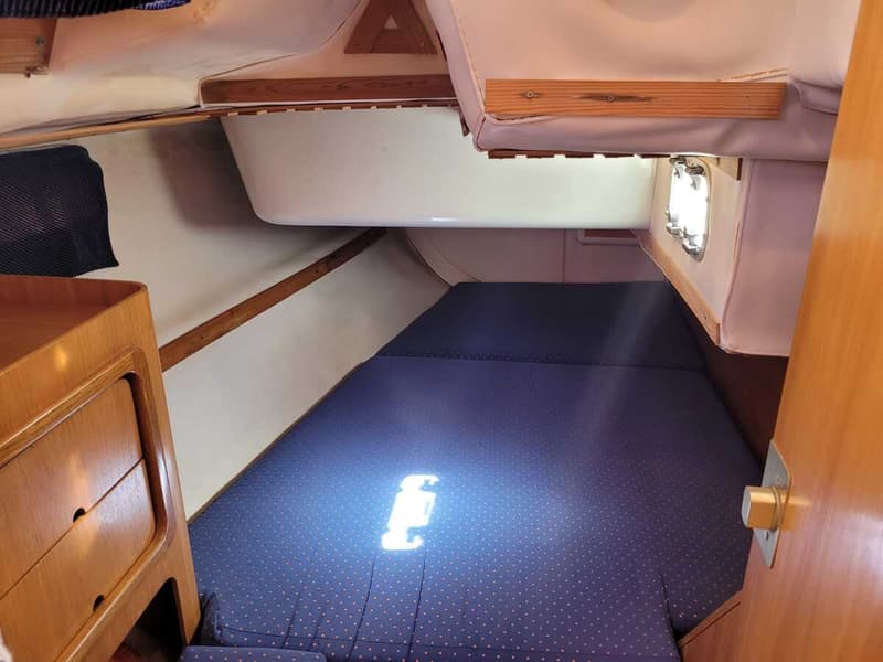 Een kajuit met een donkerblauw matras, houten kasten en een patrijspoort. — Feeling 346
