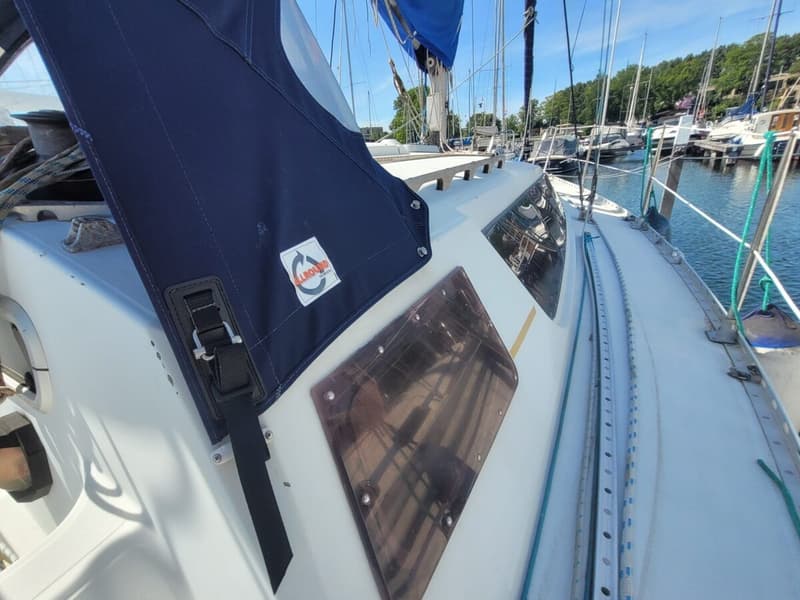 Een deel van een zeilboot met een blauwe huik, ramen en een reling, liggend in een haven. — Feeling 346