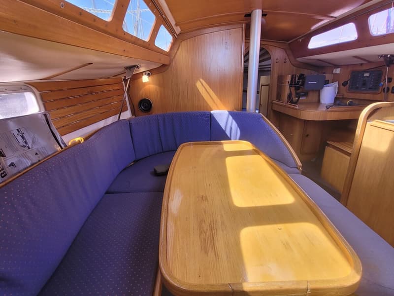 De foto toont het interieur van een boot met houten afwerking, blauwe kussens en een houten tafel in het midden.