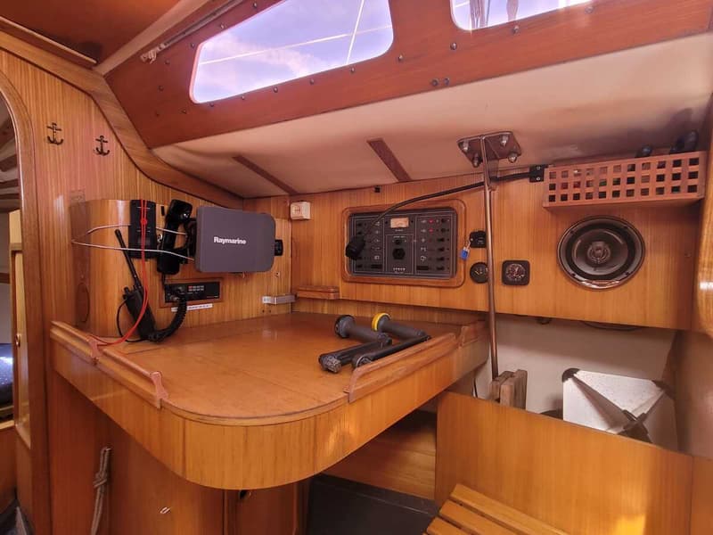 Een houten interieur van een boot met een navigatiehoek, Raymarine-apparatuur, een luidspreker en diverse meters.