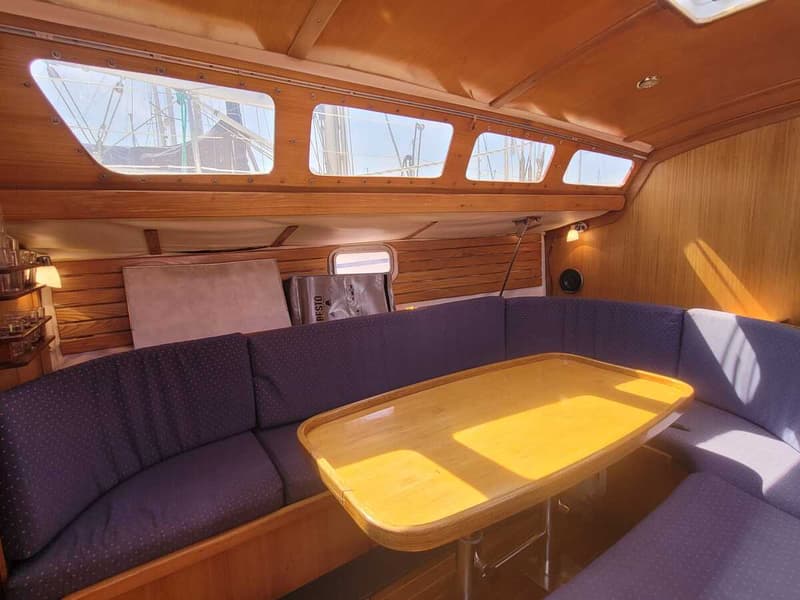 De foto toont de kajuit van een boot met houten wanden en plafond, een houten tafel en paarse banken. — Feeling 346