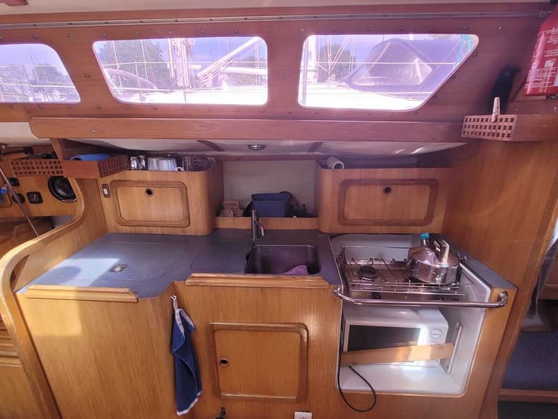 Een houten scheepsinterieur met een kombuis, inclusief een gootsteen, gasfornuis, magnetron en opbergkasten.