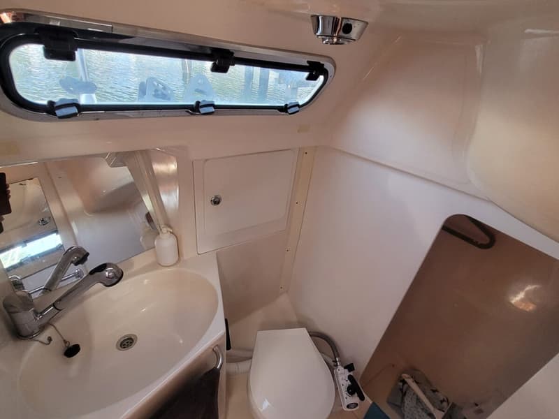 De foto toont een kajuitinterieur met een wastafel, spiegel, toilet en een raam met uitzicht op water.