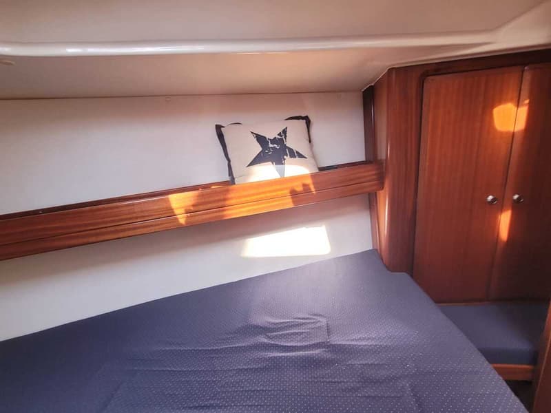 Een kajuit met een donkerblauw matras, een wit kussen met een zwarte ster, en houten kasten en afwerkingen. — Bavaria 34-2
