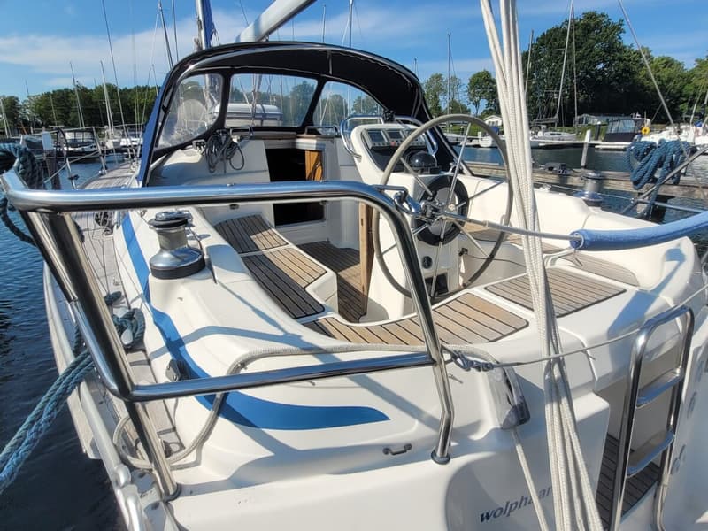 Een witte zeilboot met blauwe strepen en een teakhouten dek ligt aangemeerd in een haven. — Bavaria 34-2