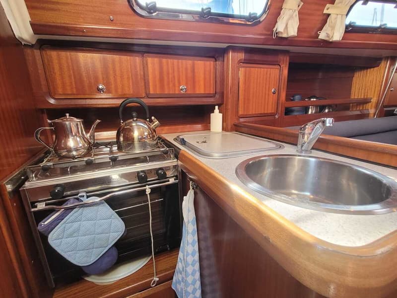 De foto toont een kombuis met een fornuis, oven, gootsteen en houten kasten.