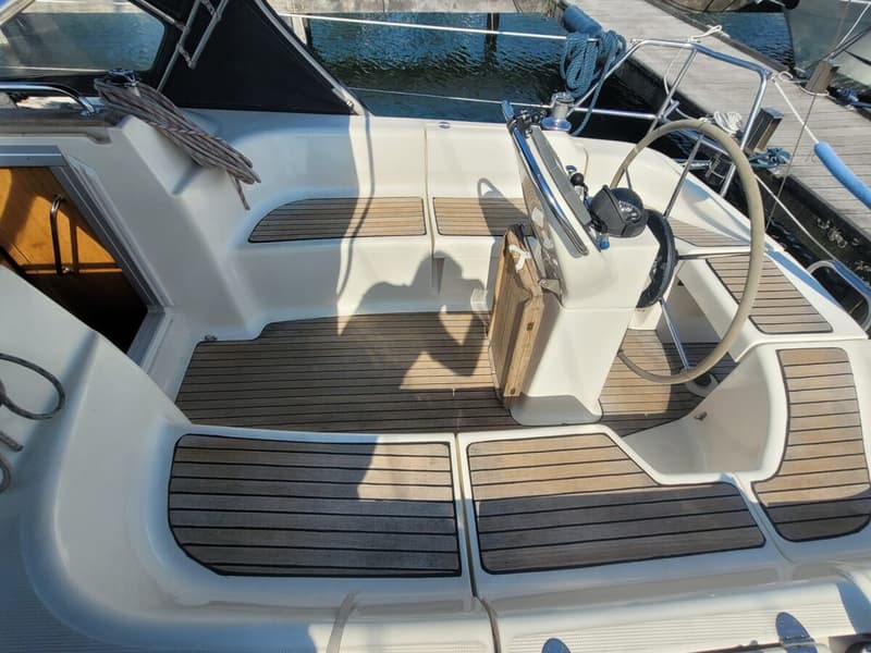 De kuip van een boot met een stuurwiel, teakhouten vloerdelen en een open kajuitingang. — Bavaria 34-2