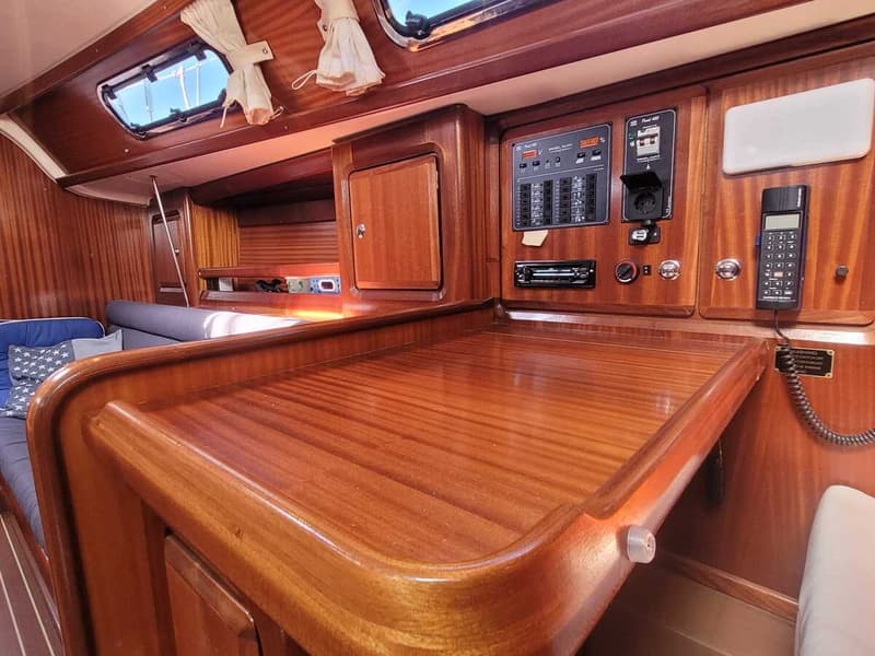 Een interieur van een boot met houten afwerking, een bed met kussens, een paneel met schakelaars en een telefoon.