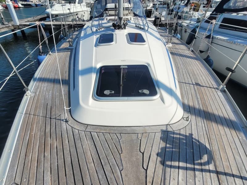 Een bovenaanzicht van het dek van een zeilboot met een houten dek en witte opbouw met ramen. — Bavaria 34-2
