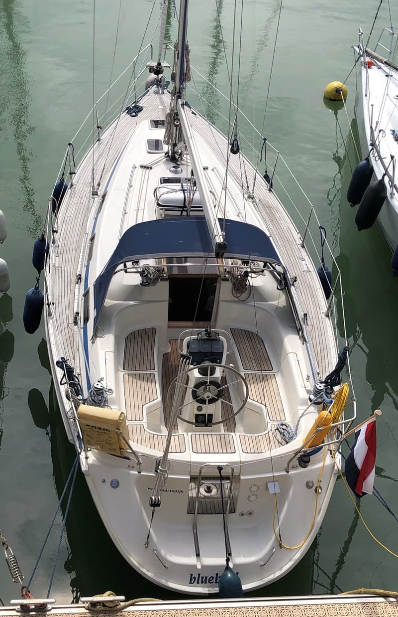 Een oranje vlag met blauwe tekst en een gestreepte vlag hangen aan de mast van een zeilboot onder een blauwe lucht.