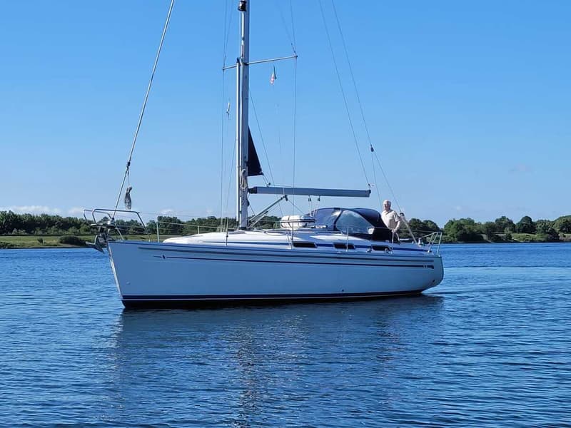 Een witte zeilboot met blauwe strepen vaart op rustig water onder een helderblauwe hemel. — Bavaria 34-2