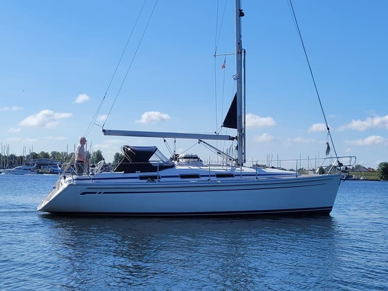 Een witte zeilboot met blauwe strepen vaart op blauw water onder een helderblauwe lucht met witte wolken. — Bavaria 34-2