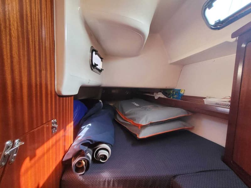 Een kajuit met een donkerblauwe matras, twee grijze kussens, een houten wand en een patrijspoort. — Bavaria 34-2