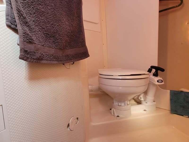 Een witte Jabsco boottoliet met een handpomp staat in een witte ruimte met een grijs handdoek.