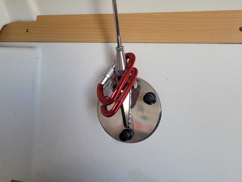 Een detailfoto van een zilverkleurige metalen plaat met twee zwarte knoppen, waaraan twee rode karabijnhaken hangen.