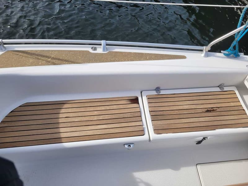 De foto toont een deel van een witte boot met houten dekpanelen en een reling, met water op de achtergrond. — Etap 21i