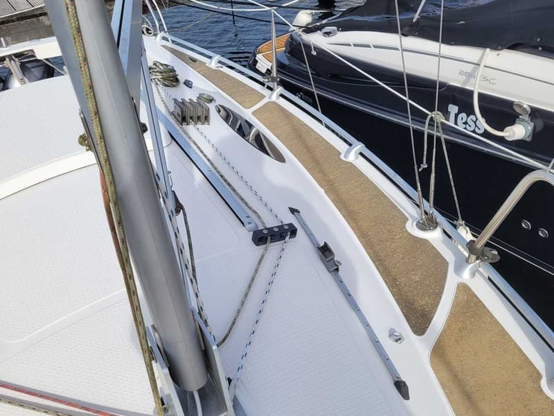 Een bovenaanzicht van het dek van een witte zeilboot met een mast, lijnen, blokken en een bruine antislipmat. — Etap 21i