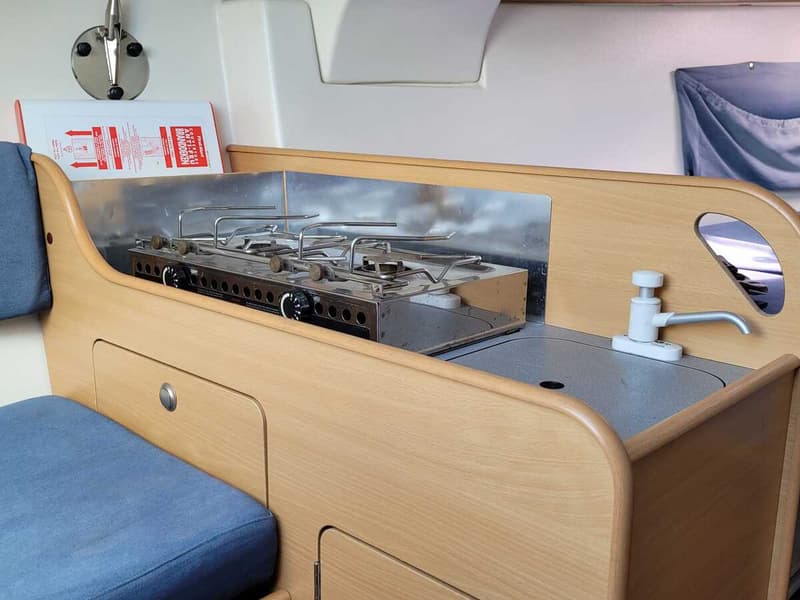 Een bootkeuken met een tweepits gasfornuis, een spoelbak met kraan en een branddeken aan de muur.