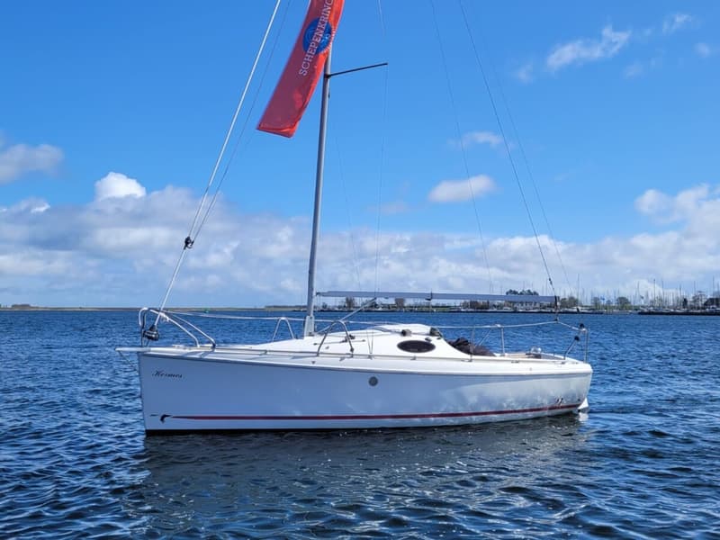 Een witte zeilboot met de naam "Hermes" en een rode vlag met "SCHEPENKRING" erop, drijft op het water. — Etap 21i