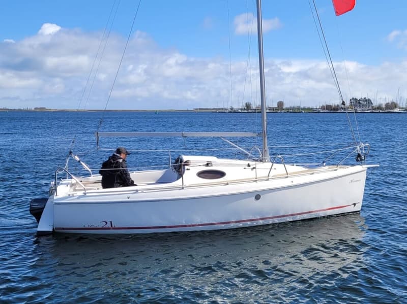 Een witte zeilboot met een rode streep op de romp vaart op blauw water onder een heldere hemel. — Etap 21i