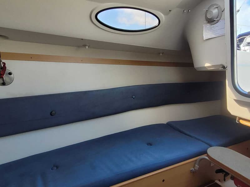 De foto toont een interieur van een boot met blauwe kussens op de banken en een ovaal raam in het plafond. — Etap 21i