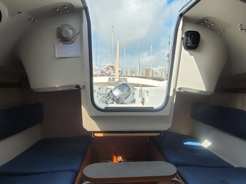 De foto toont het interieur van een kajuit met blauwe kussens en een tafel, uitkijkend op een buitenboordmotor en andere…