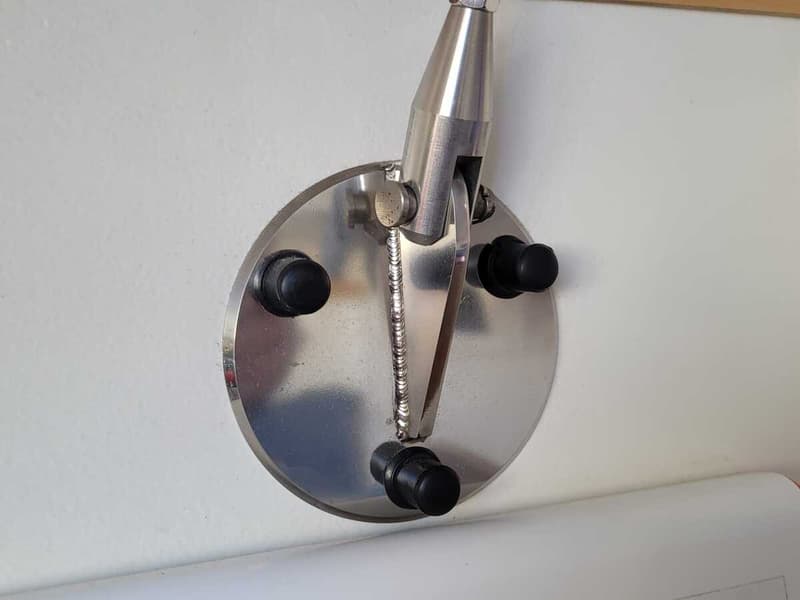Een close-up van een ronde, zilverkleurige metalen plaat met drie zwarte knoppen en een metalen beugel.