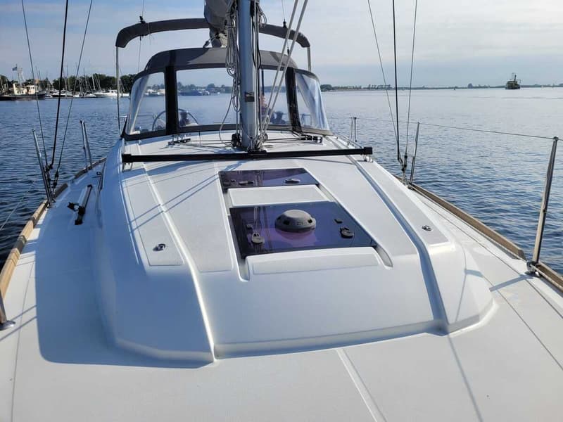 Een witte zeilboot met een donkere buiskap en ramen, liggend op het water met andere boten op de achtergrond.