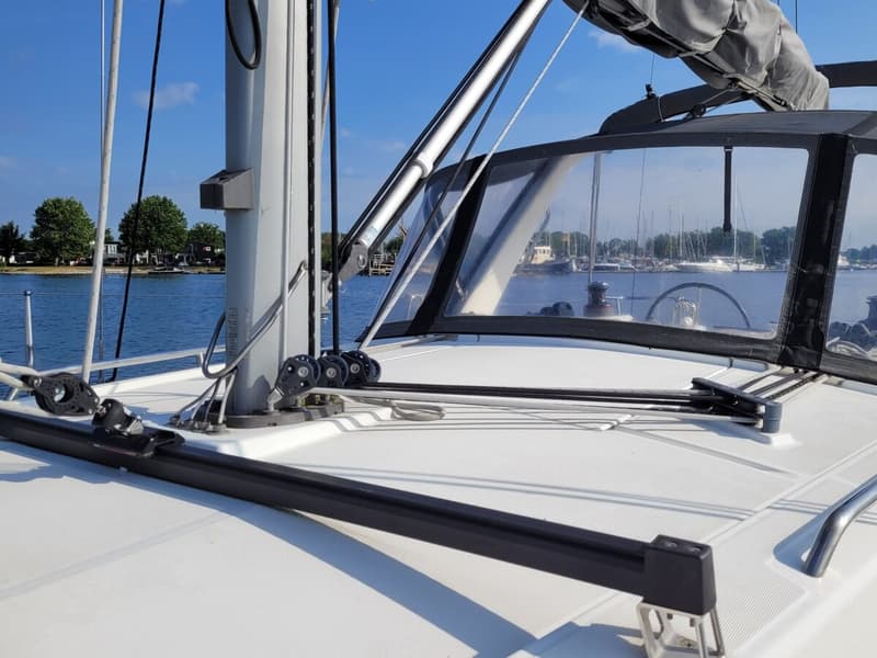 Een dek van een zeilboot met mast, lijnen, blokken en een buiskap, met water en land op de achtergrond. — Beneteau Oceanis 35