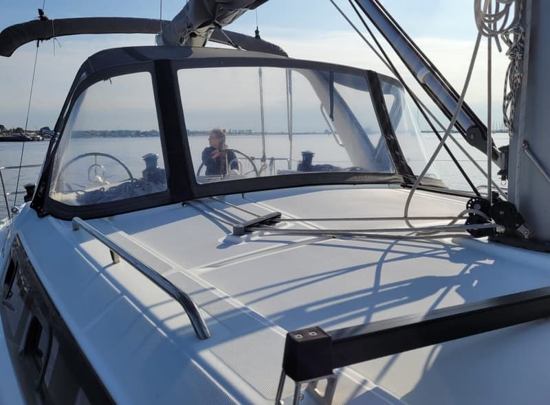 Een vrouw zit aan het roer van een zeilboot, gezien door de voorruit van de kajuit. — Beneteau Oceanis 35