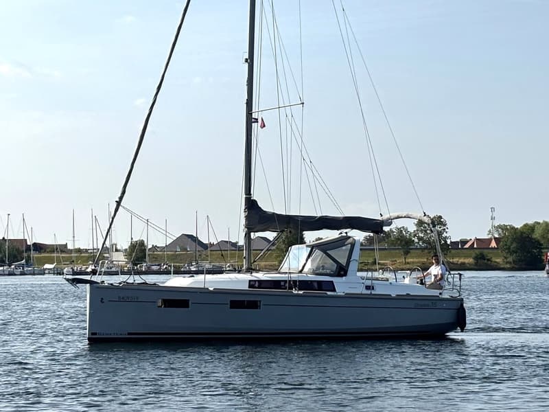 Een grijze zeilboot met een zwarte mast en zeil vaart op het water, met een persoon aan het roer. — Beneteau Oceanis 35