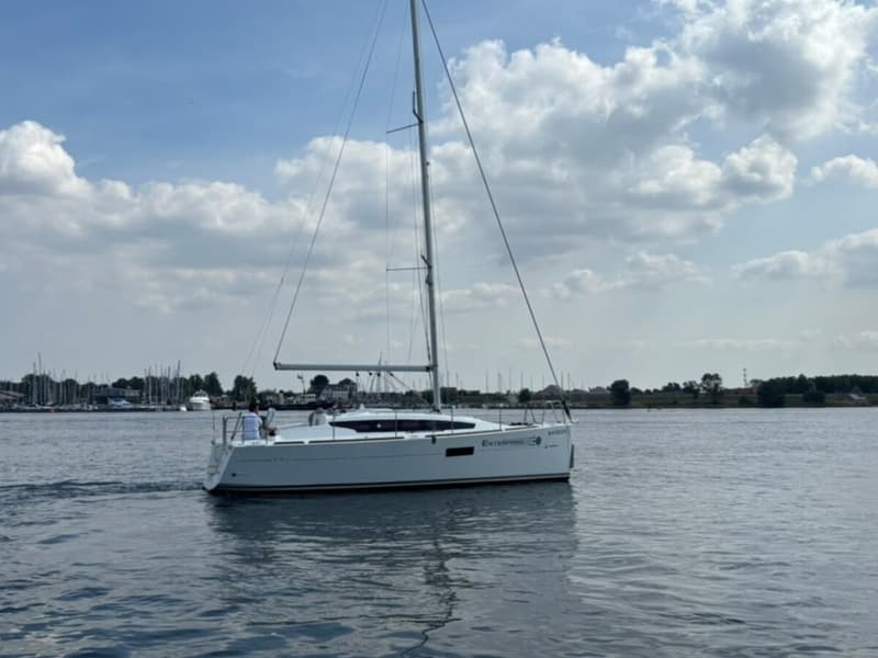 Een witte zeilboot met de naam "ENTERPRISE" vaart op rustig water onder een deels bewolkte hemel. — Jeanneau Sun Odyssey 319