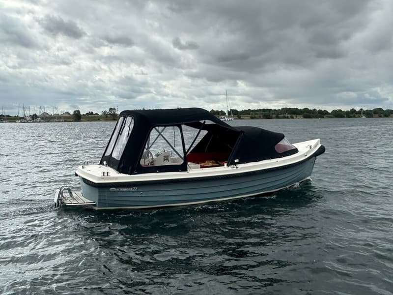 Een blauw-witte Interboat 22 met zwarte kap vaart op een meer onder een bewolkte hemel.