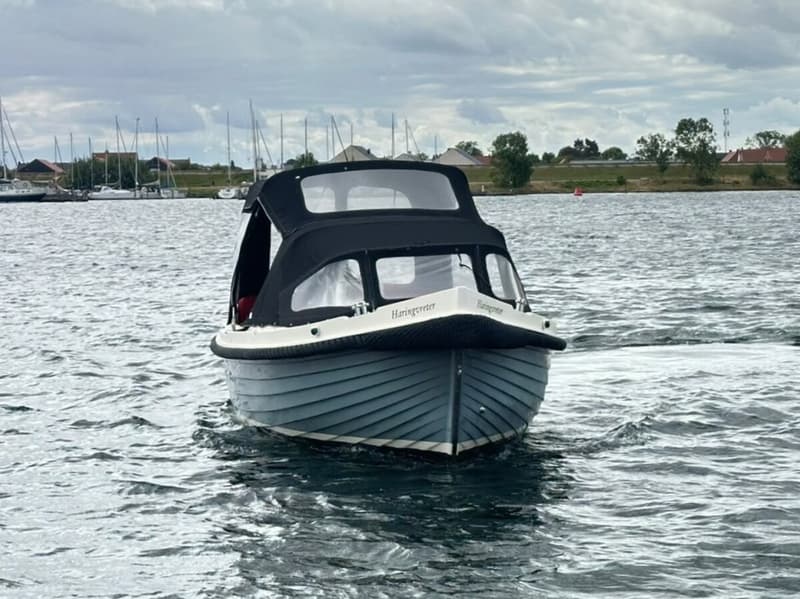 Een blauwe boot met een zwarte kap en de naam "Haringvreter" vaart op water met een bewolkte lucht erboven. — Interboar 22