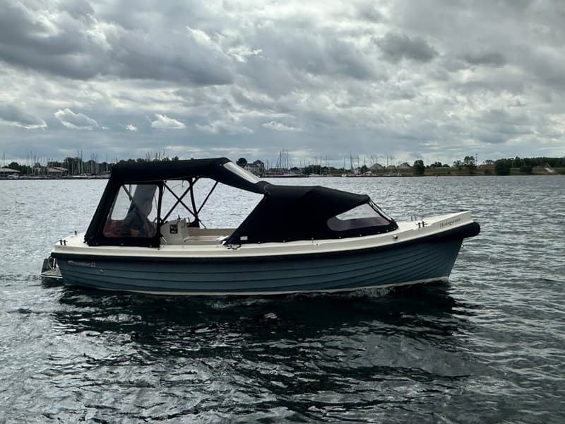 Een blauw-witte sloep met een zwarte kap vaart op water onder een bewolkte hemel. — Interboar 22