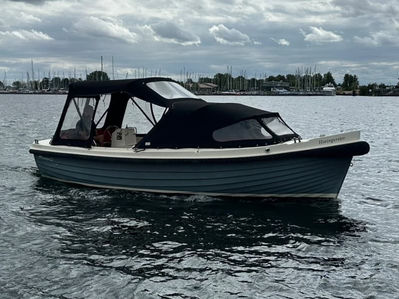 Een blauw-witte sloep met een zwarte kap vaart op het water onder een bewolkte hemel. — Interboar 22