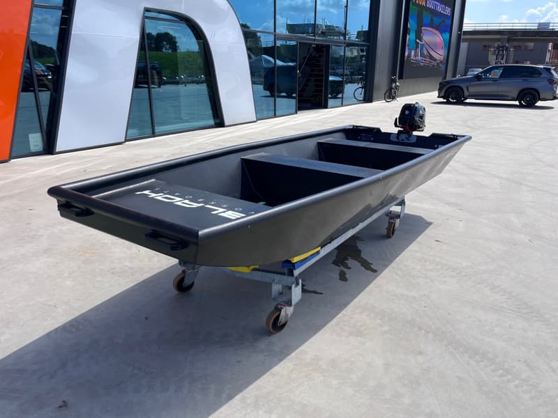Een donkergrijze boot met een buitenboordmotor staat op een kar met wielen voor een gebouw — Black work boats Black Jon 400