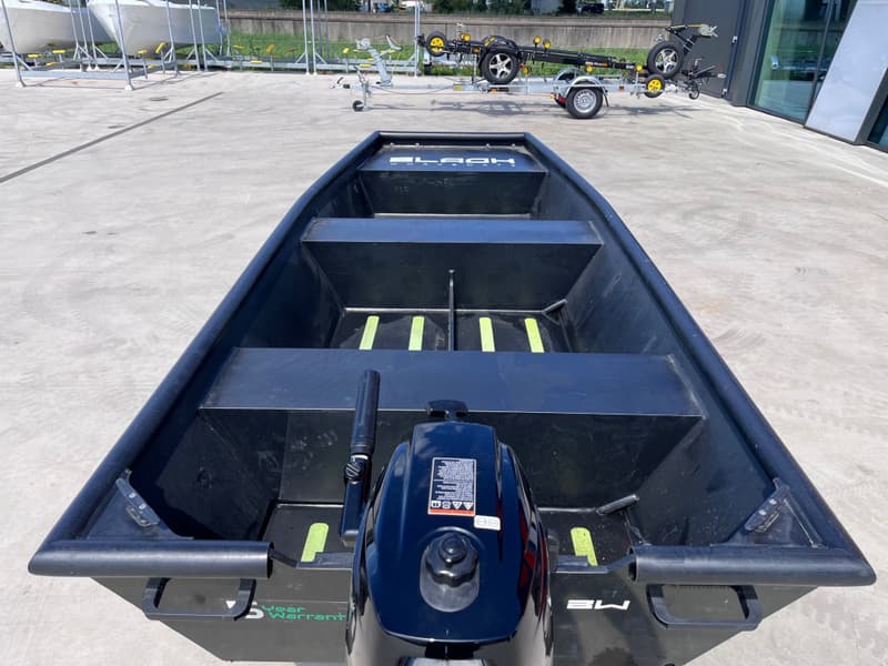 Een zwarte open boot met een buitenboordmotor staat op een betonnen ondergrond, met een — Black work boats Black Jon 400