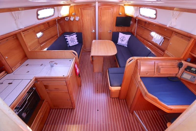 De foto toont het interieur van een boot met houten afwerking, een kombuis, zithoeken en een navigatiehoek.
