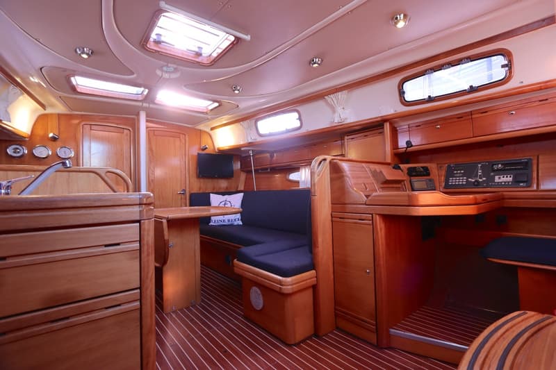 De foto toont het interieur van een boot met houten afwerking, een zithoek, een kombuis en navigatieapparatuur.