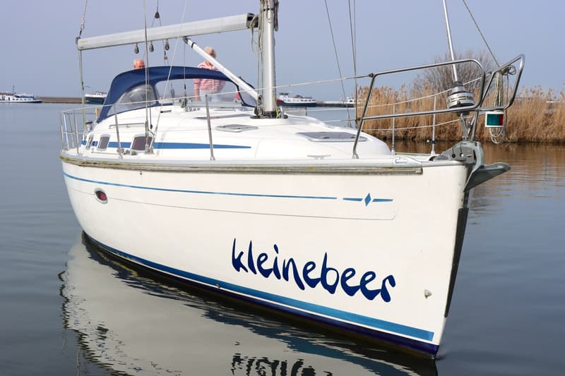 Een witte zeilboot met de naam "kleinebeer" in blauwe letters op de boeg, dobbert op rustig water. — Bavaria 37-3 Cruiser
