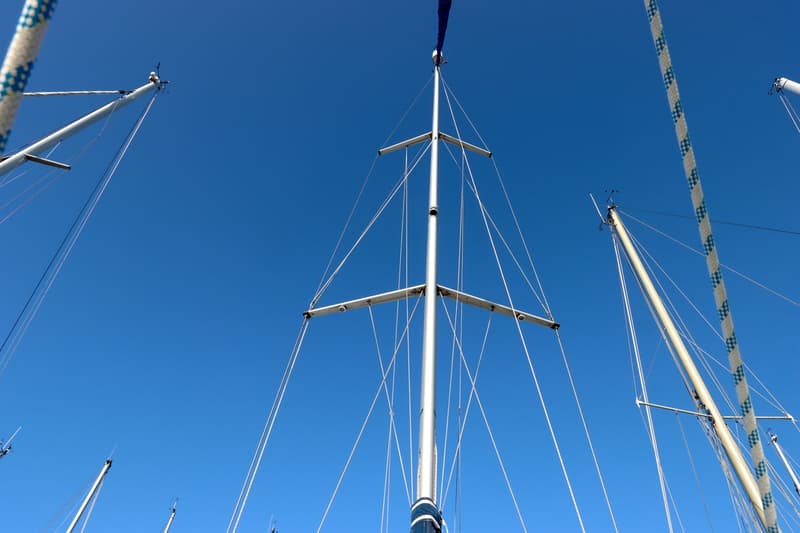 Een detailfoto van de mast en verstaging van een zeilboot, met een helderblauwe lucht op de achtergrond.
