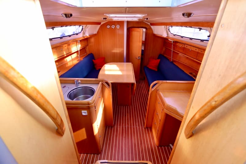 De kajuit van een boot met houten interieur, blauwe banken, een tafel en een gootsteen. — Bavaria 31