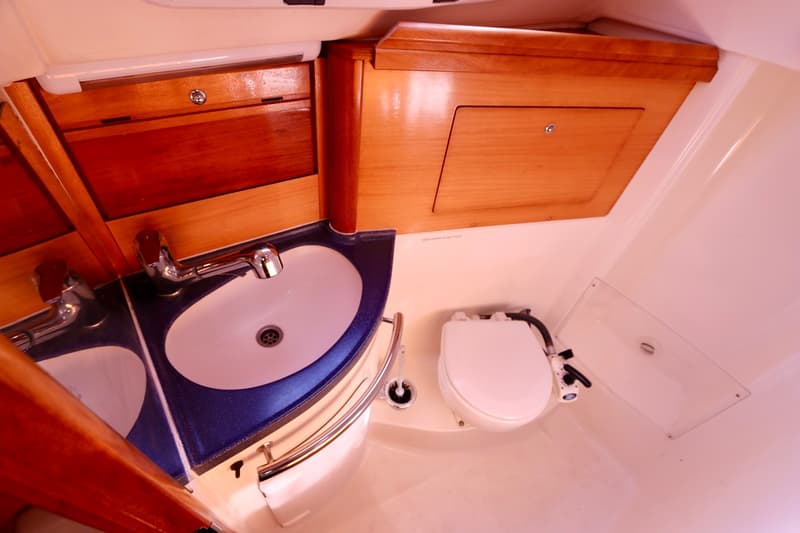 De foto toont een badkamerinterieur met een witte wastafel in een blauw aanrechtblad, een toilet en houten kasten.