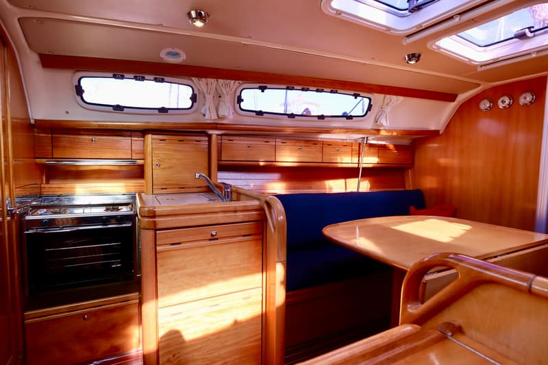De foto toont het interieur van een boot met een houten afwerking, een kombuis, een zithoek en patrijspoorten. — Bavaria 31
