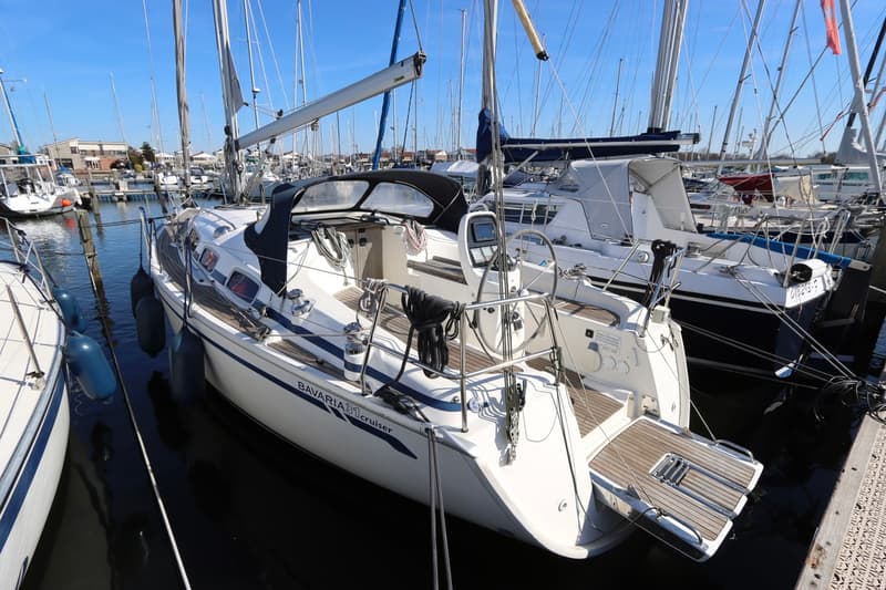 Een witte zeilboot met de tekst "BAVARIA 31 cruiser" ligt afgemeerd in een haven vol met andere boten. — Bavaria 31
