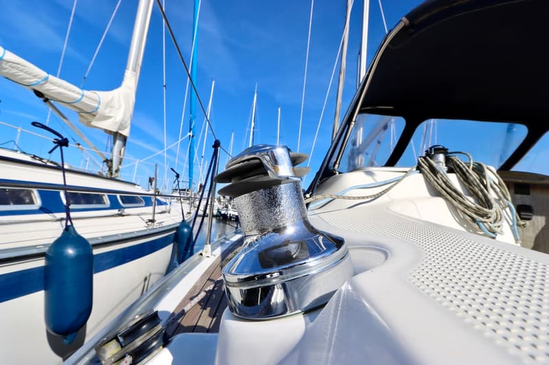 Een glimmende lier op het dek van een zeilboot, met op de achtergrond een blauwe lucht en andere boten. — Bavaria 31