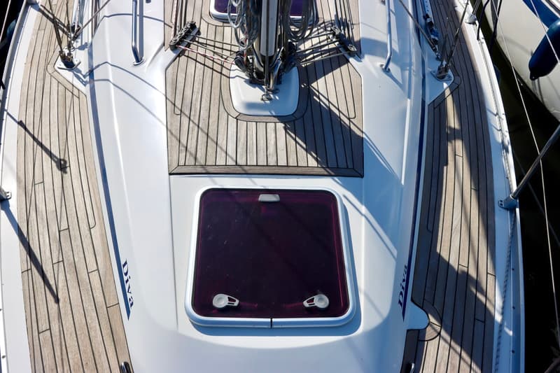 Een bovenaanzicht van het dek van een zeilboot met houten planken, een luik en de naam "Diva" op de zijkant. — Bavaria 31