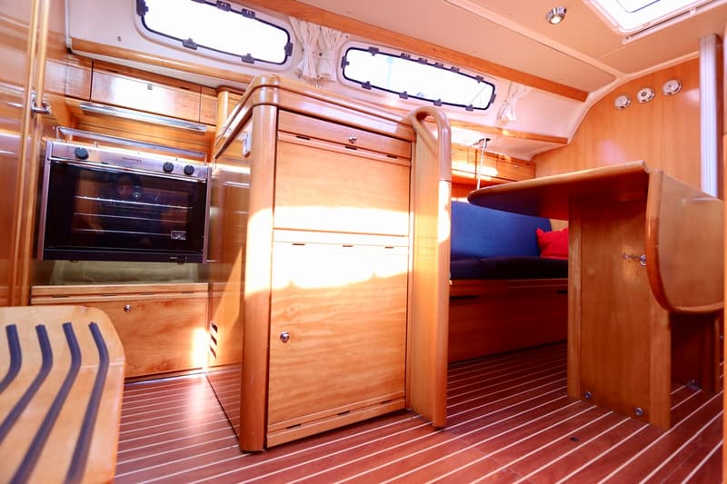 De foto toont het interieur van een boot met een oven, houten kasten, een tafel en een blauwe bank. — Bavaria 31