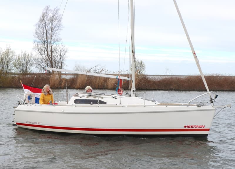 Een witte zeilboot met rode strepen en de namen "ETAP 23iL" en "MEERMIN" vaart op water met twee personen aan boord.